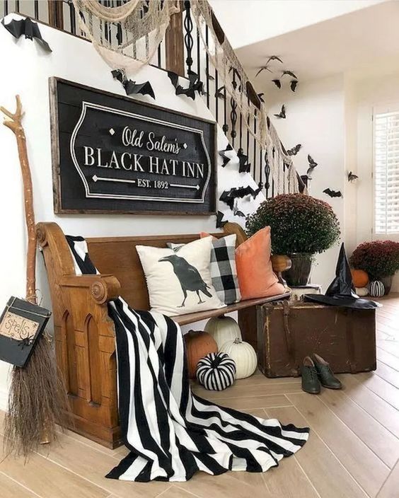 A gorgeous Halloween entryway with large pumpkins, black and white fabric, a witch broom, hat, shoes and some bats
