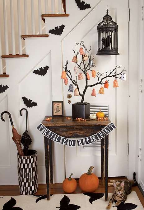 a Halloween entryway with bats, a blackbird in a cage, orange pumpkins, a black and white bunting, a Halloween tree with ornaments
