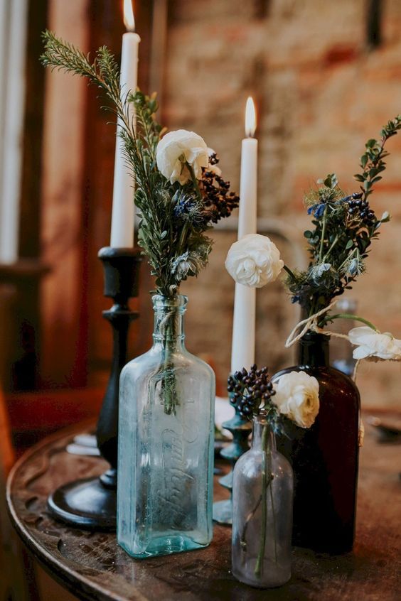 a chic Halloween centerpiece of glass bottles with blooms and dried greenery plus some tall candles