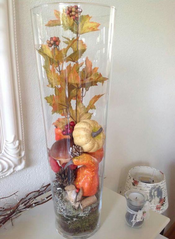 a fall decoration made of a tall vase filled with pinecones, gourds, pumpkins and leaves - all of them are faux