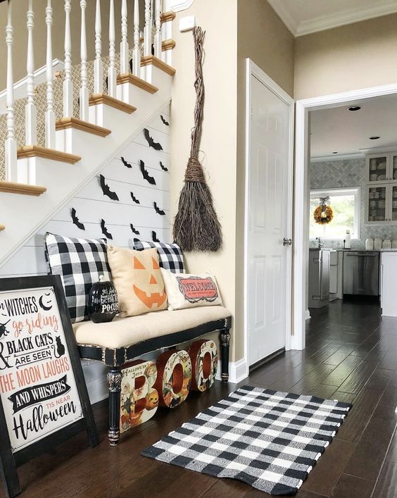 a Halloween entryway with letters, plaid elements, a broom of twigs, a sign and some pumpkin pillows