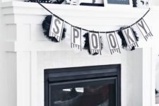 21 a black and white Halloween mantel with a garland, a wreath, a sign, some paper fans, a blackbird and some spiders