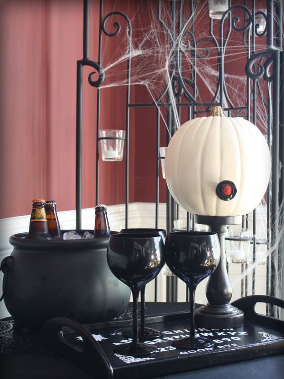 a simple drink station with a white pumpkin as a bottle, some black glasses and a cauldron with ice and bottles