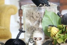 23 a glass jar with hay and skulls, some faux pumpkins, greenery and a blackbird on top for Halloween