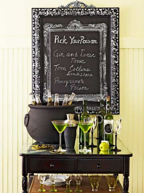 a stylish Halloween drink station with green bottles and sheer glasses, green drinks and a cauldron with bottles plus a sign