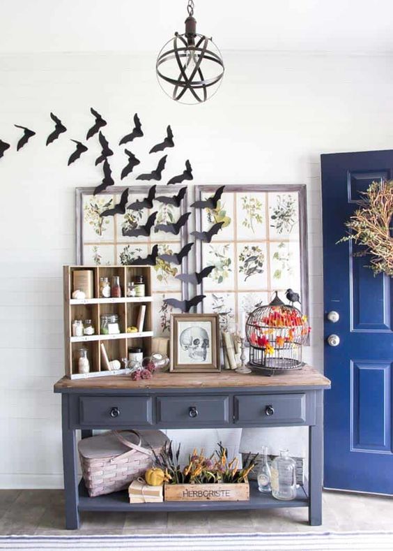 a vintage Halloween entryway with bats, a skull sign and a black cage with a faux blackbird create a mood here