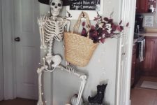 26 Halloween entryway decor with a skeleton, lights, a candle lantern, a create with pumpkins and a straw bag with dark blooms