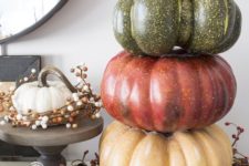 26 a stack of faux pumpkins placed on a wreath of vines, berries and nuts is a durable fall decoration