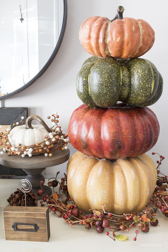 a stack of faux pumpkins placed on a wreath of vines, berries and nuts is a durable fall decoration