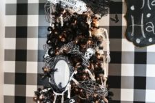 a black Halloween tree decorated with lights, candy corns, mirrors, skulls, a sign and skeletons