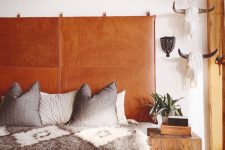 a boho bedroom with an amber leather suspended headboard, a bed with printed bedding, a skull gallery wall