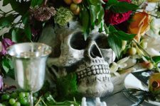 a bold Halloween centerpiece of a skull as a vase, greenery, bold blooms and fruit is a lovely idea