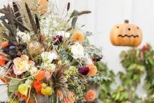 a bright rustic Halloween centerpiece with fresh peachy, orange and dried blooms, dark and usual foliage and greenery