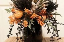 a catchy Halloween flower arrangement of a black jar, greenery, black elements, orange pumpkins and blooms