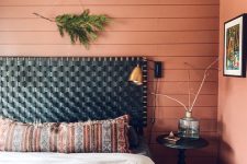 a catchy boho bedroom with a salmon pink accent wall, a bed with a black woven headboard, printed bedding, a black nightstand