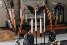 a cluster Halloween centerpiece of a black owl, a black heart vase with feathers, candles in candleholders and candles