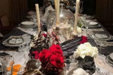 a cluster Halloween centerpiece of skulls, red and white blooms and tall candles is a cool and bold idea