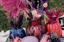 a colorful Halloween centerpiece of a pink skull, pink and black vases with feathers and leaves and a small white pumpkin