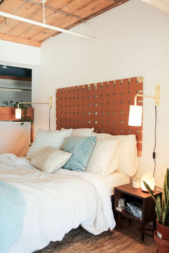 A mid century modern bedroom with an amber leather headboard, blue and white bedding, nightstands and sconces