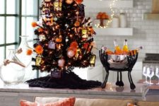 a mini black Halloween tree decorated with white and orange ornaments, lights and a scary pumpkin head doll on top