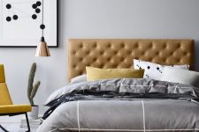 a modern bedroom with an amber leather bed, grey bedding, a yellow rocker chair, a copper pendant lamp