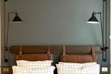 a modern bedroom with grey walls, a bed with brown leather suspended headboard, printed bedding and black lamps