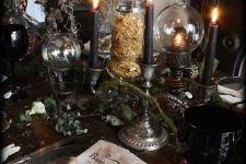 a moody Halloween centerpiece of black candles in candleholders, some lamps and greenery to rock