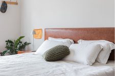 a neutral modern bedroom with a bed and a brown leather headboard, neutral bedding, nightstands, table lamps and greenery