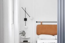 a refined modern bedroom with a bed and an amber leather suspended headboard, neutral bedding, floating nightstands and lamps