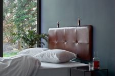 a serene bedroom with dark walls, a bed with a brown suspended headboard, white bedding, nightstands and greenery