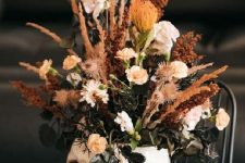 a skull with neutral blooms, greenery and dried grasses is a cool and pretty Halloween centerpiece