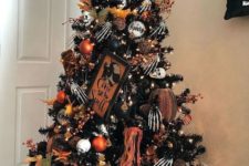 a spooky black Halloween tree decorated with skeleton hands, pumpkins, black and orange ornaments, a sign and lights