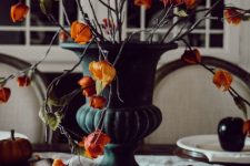 a stylish Halloween centerpiece of a black urn with orange seed pods is a super catchy and lovely idea