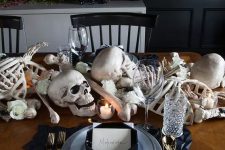 a stylish Halloween tablescape with bones, skulls, candles, white blooms, black geometric placemats and plates, gold cutlery