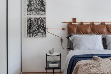a stylish bedroom with a bed and a brown leather suspended headboard, a bed with contrasting bedding, a nightstand and abstract art