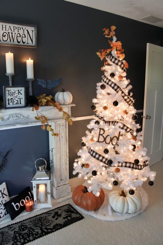 a white Halloween tree decorated with black and orange ornaments, a checked garland, lights and two large pumpkins under it