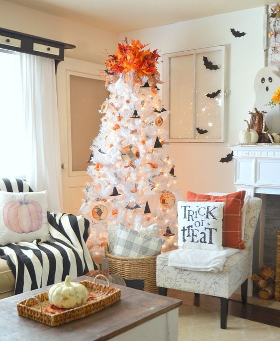 a white Halloween tree with lights, cardboard hats, fabric ornaments and a bold orange topper of leaves