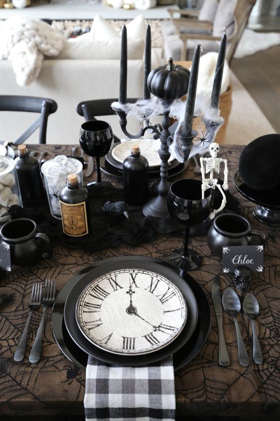 an elegant vintage Halloween centerpiece with black candles in a candelabra, black apothecary bottles and cups as cauldrons