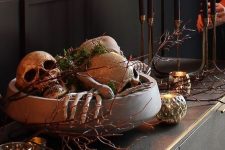 refined Halloween decor with a bowl filled with skeleton hands, skulls and moss, branches, candles around is amazing