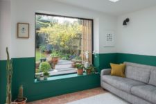 02 The living room features colo color blocking – an emerald and white wall and it is filled with light through a window and a skylight