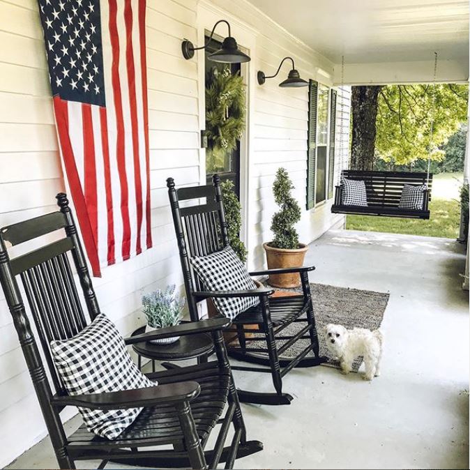 The porch is done with cozy black rockers, a hanging daybed, some potted greenery and lamps over the door