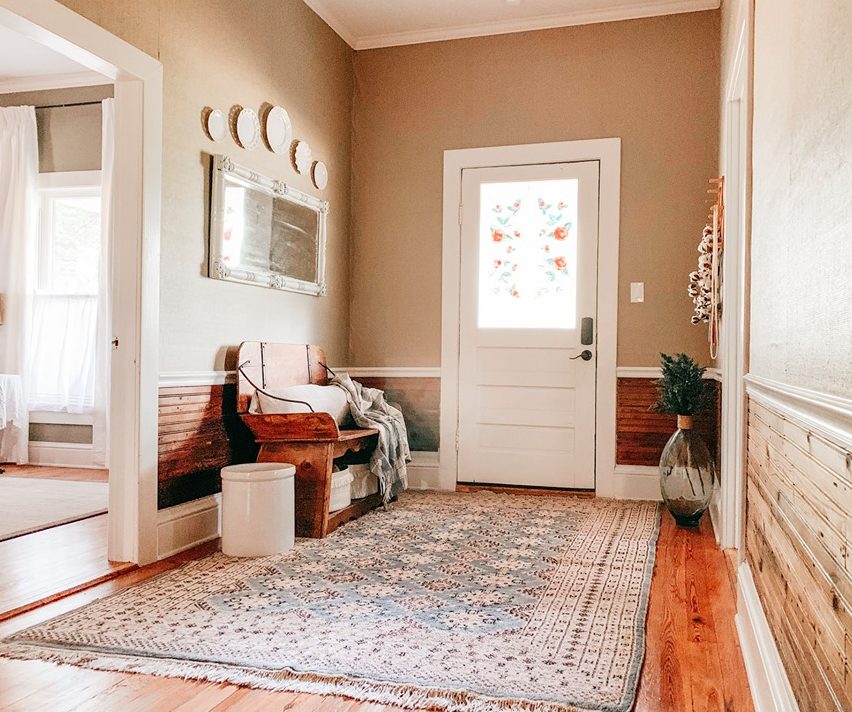 The entryway is cozy and simple, with a printed rug, some vintage plates and a vintage wooden bench