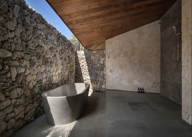 the bathroom with a shower and a tube of stone is indoor-outdoor with a stone wall that keeps privacy and a roof over it