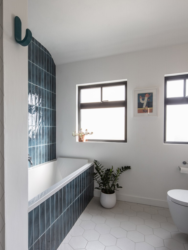 the bathroom is clad with teal tiles on the wall  and hexagon ones on the floor and features windows