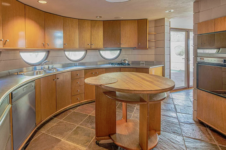 The kitchen is done with wooden cabinets of various shades coming in an arch and a round kitchen island in the center