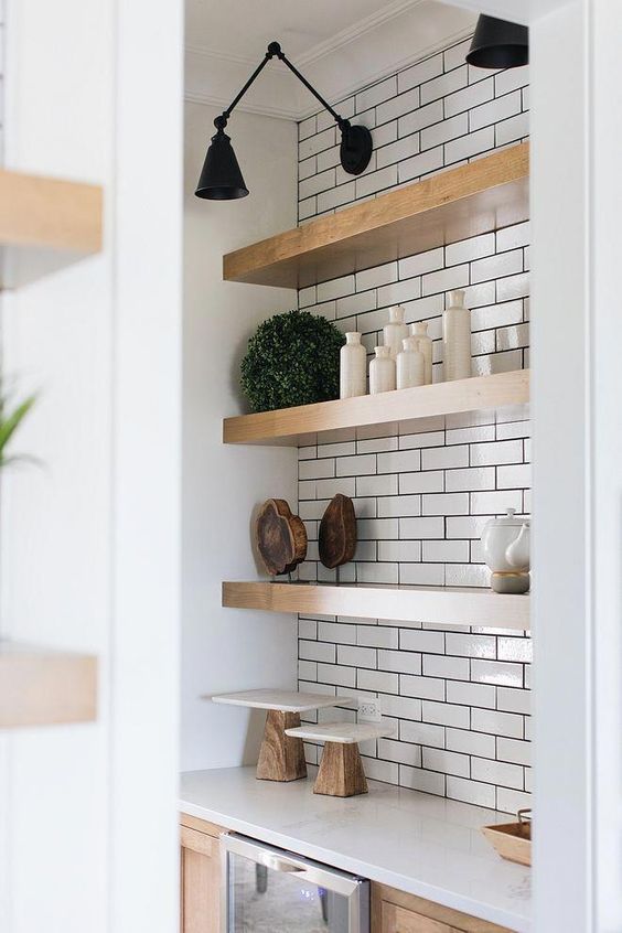 thick wooden shelves in a white tile niche look warming up and give a slight farmhouse feel to the space