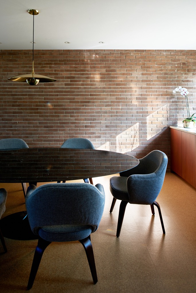 The dining space features a dark mirror table, blue chairs and a faux brick wall for a catchy look