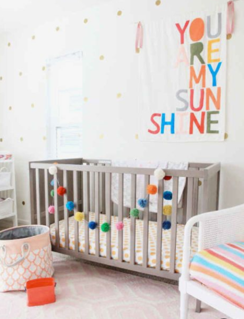 An all neutral nursery with a colorful artwork, a bright pompom garland and a colorful striped chair