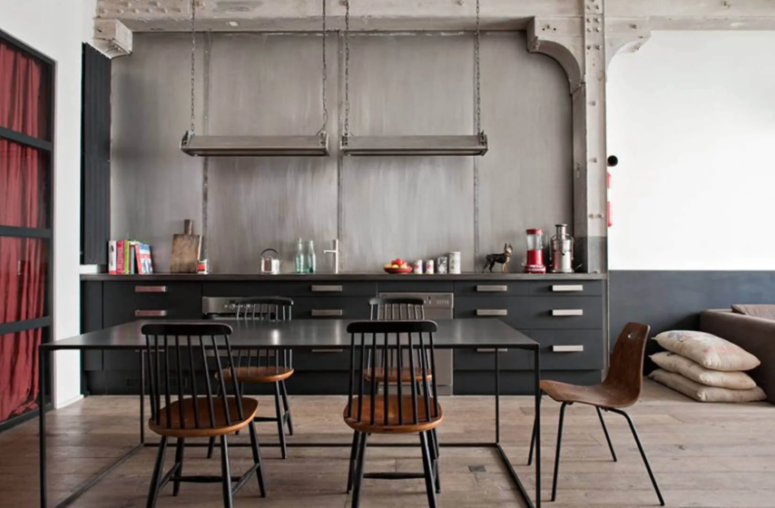a black industrial kitchen made bolder with a concrete wall and metal countertops, handles and lamps