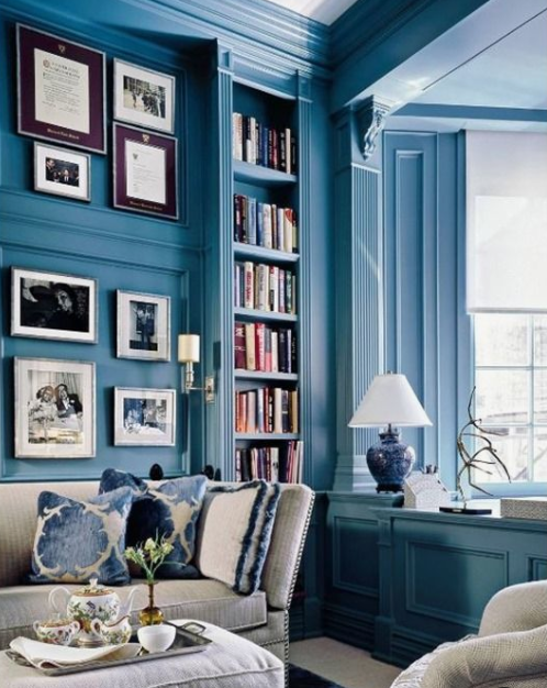 a bright blue home office and library with built-in bookshelves and elegant white furniture and artworks